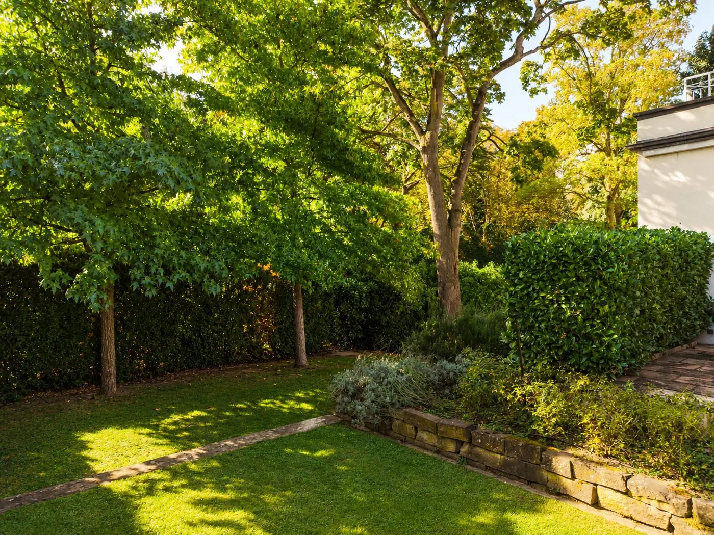 Gepflegter Garten mit Bäumen, Hecke und Steinmauer